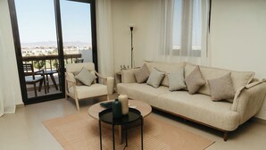 Un salon comprenant un canapé, des fauteuils, une table basse et une vue sur l’extérieur, visible à travers une porte vitrée.