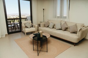 Una sala de estar con sofá, sillones, una mesa de centro y vistas a través de un ventanal.