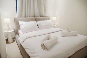 Una cama bien hecha con sábanas blancas, dos lámparas de noche y toallas enrolladas.