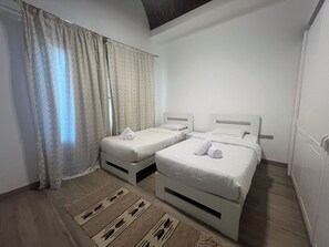 A hotel room with two beds, a window with curtains, a patterned rug, and a wooden floor. - Cozy South Marina 2Bdr with Pool Access (Red Sea)
