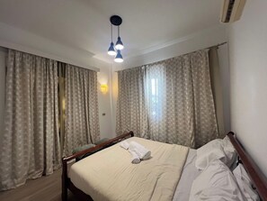 Une chambre d’hôtel avec un lit, des rideaux, une lampe fixée au mur et un ventilateur de plafond.