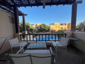 A balcony with a pool view, white furniture, and a pergola structure. - Cozy South Marina 2Bdr with Pool Access (Red Sea)