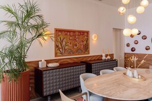 A dining area with a round table, cushioned seating, a large potted plant, a wall-mounted light fixture, and a decorative wall piece. - The Reef House Luxury Waterfront Villa (El Gouna Hurghada)