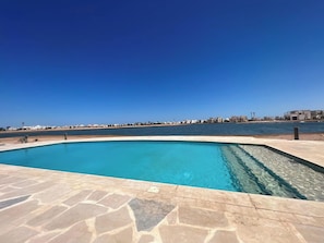 A rectangular swimming pool with clear blue water, surrounded by a stone deck.