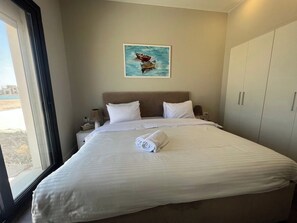 A hotel room with a large bed, a painting on the wall, and a view through the window.