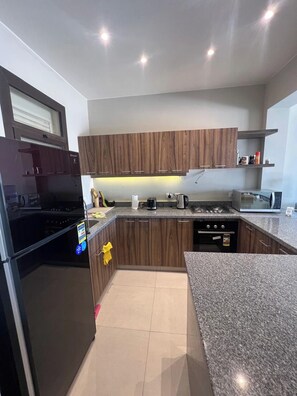 A modern kitchen with wooden cabinets, a granite countertop, and built-in appliances including a stove, oven, and microwave. - Cyan Luxe Retreat 3BR Townhouse with Lagoon View (Hurghada 2)