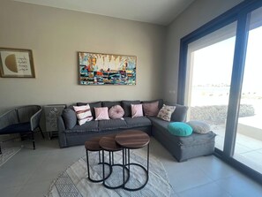 Een moderne woonkamer met een hoekbank, een bijzettafeltje en een groot raam.