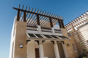 Un edificio con una estructura de pérgola de madera, paneles solares y un cielo azul despejado.