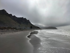A beach with a rocky cliff and a person fishing.