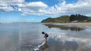 En strand med en person stående i lavt vand, en klar himmel og fjerne bakker.