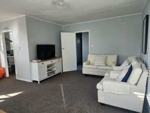 A living room with a white sofa, a TV on a wooden stand, and a door leading to another room.