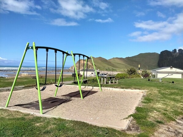 A playground with swings, a picnic table, and a view of the ocean and hills.
