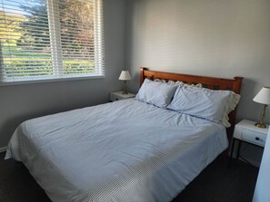 A neatly made bed with a striped bedspread, two bedside lamps, and a window with blinds.