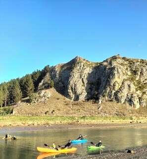 Kayakers on a calm river with a rocky mountain in the background. - Classic Kiwi bach escape with cliff views (Kairākau)