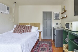 A compact bedroom with a bed, a small kitchenette, a door, and a wall-mounted air conditioner. - Walk to University & 4th Ave: Tucson Studio (Tucson)