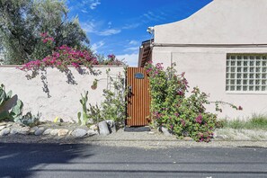 A building with a stucco exterior, a wooden gate, and pink flowering plants. - Walk to University & 4th Ave: Tucson Studio (Tucson)