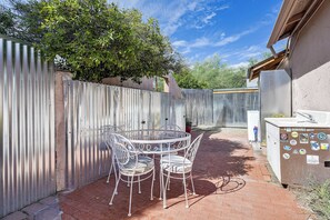 A fenced backyard with a metal table and chairs, a refrigerator, and a wooden structure. - Walk to University & 4th Ave: Tucson Studio (Tucson)