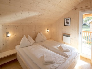 Ein Zimmer mit Holzwänden und einem Bett mit weißen Leinentüchern. An der Wand hängt ein Bild, und das Fenster bietet einen Blick nach draußen.