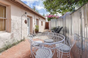 Eine Terrasse mit einem runden Tisch, Stühlen, einem Blumentopf und einem Metallzaun.