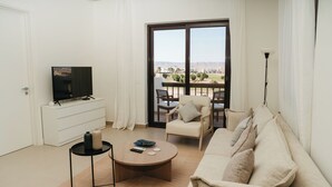 Una sala moderna con televisor de pantalla plana, un sofá, una mesa de centro y un balcón con vistas.