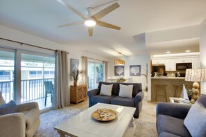 A modern living room with a large window, a ceiling fan, and a kitchen area with a bar. - Access to Pool & Sanibel Beach: Resort-Style Condo (Sanibel)