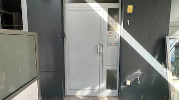Een grijze deur met een hendel, een klein bedieningspaneel en een geel bord met cijfers.