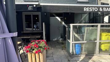 Een gebouw met een bord waarop 'RESTO & BAR' staat en een houten plantenbak met rode bloemen ervoor.