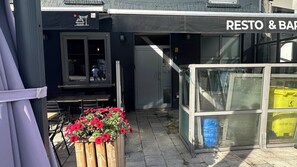 Een gebouw met een bord waarop 'RESTO & BAR' staat en een houten plantenbak met rode bloemen ervoor.