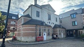 Een historisch gebouw met een stenen gevel, een hoingang en een straat met kinderaardewerktegels.