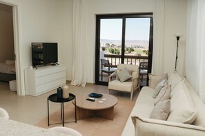 Una sala de estar moderna con una televisión de pantalla plana, un sofá, una mesa de centro y un balcón con mobiliario exterior.