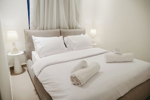 A neatly made bed with white linens, two bedside lamps, and rolled towels. - 1 BR Ancient Sands Residence (Hurghada)