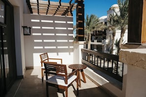 A balcony with a wooden table and chairs, a white wall with a wooden slat design, and a view of palm trees and a building with a dome. - 1 BR Ancient Sands Residence (Hurghada)
