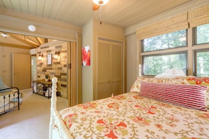 A bedroom with a bed, a table with chairs, a wardrobe, and a window with a view of trees.