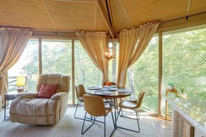 A room with a round table, chairs, a sofa, and a view of trees through large windows. - Boater’s Paradise! Hiwassee Lake Treetop Retreat (Murphy)