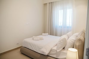 Habitación de hotel con cama, lámpara de noche y ventana con cortinas.