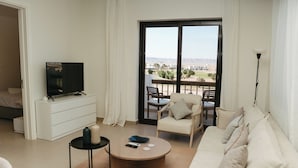 Una sala de estar moderna con una televisión de pantalla plana, un sofá, una mesa de centro y un balcón con mobiliario exterior.