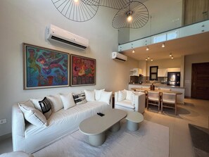 A modern living room with a white sofa, two paintings, a dining area with a table and chairs, and a kitchen in the background. - Bohemian-Style 3BR Townhouse in Shedwan, El Gouna. (Hurghada)