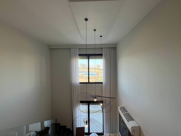 A modern interior with a large window, a staircase, and a unique light fixture.
