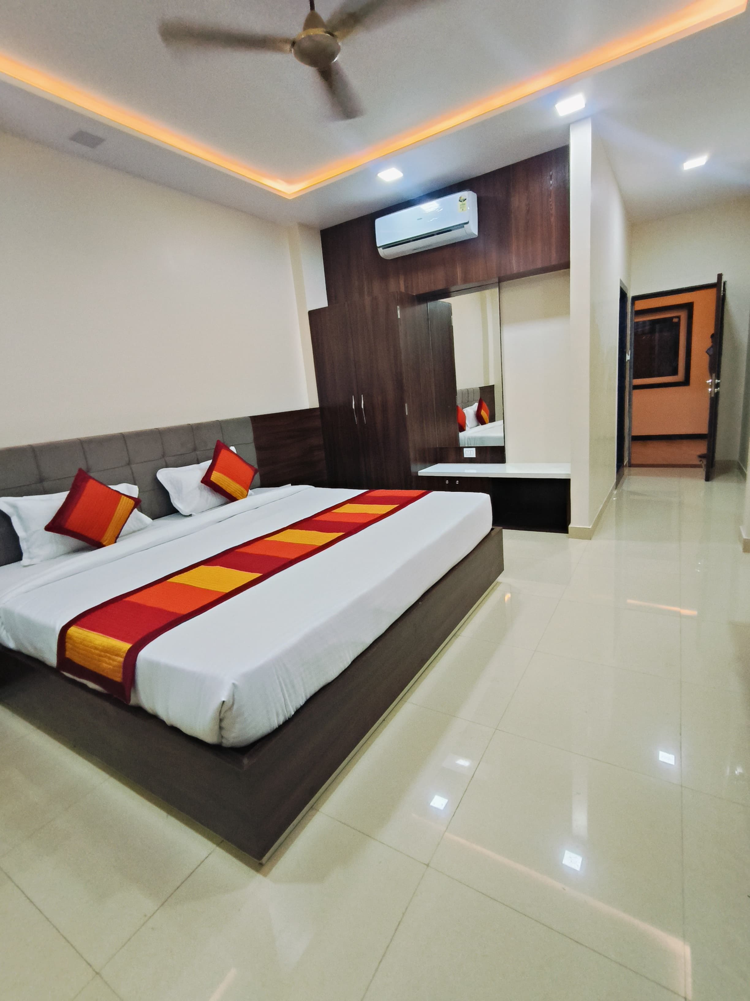 A hotel room with a bed, a ceiling fan, an air conditioning unit, and a bathroom door.