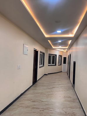 A hallway with a tiled floor, recessed lighting, and doors leading to rooms.