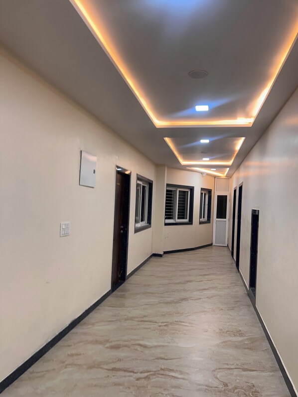 A hallway with a tiled floor, recessed lighting, and doors leading to rooms. - Papaya Leaf Stay (Nathdwara)