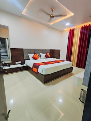 Quarto de hotel com cama, mesa de cabeceira e ventoinha no teto.