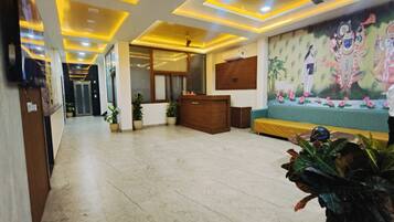 A hotel lobby with a reception desk, a ceiling fan, and a mural on the wall.
