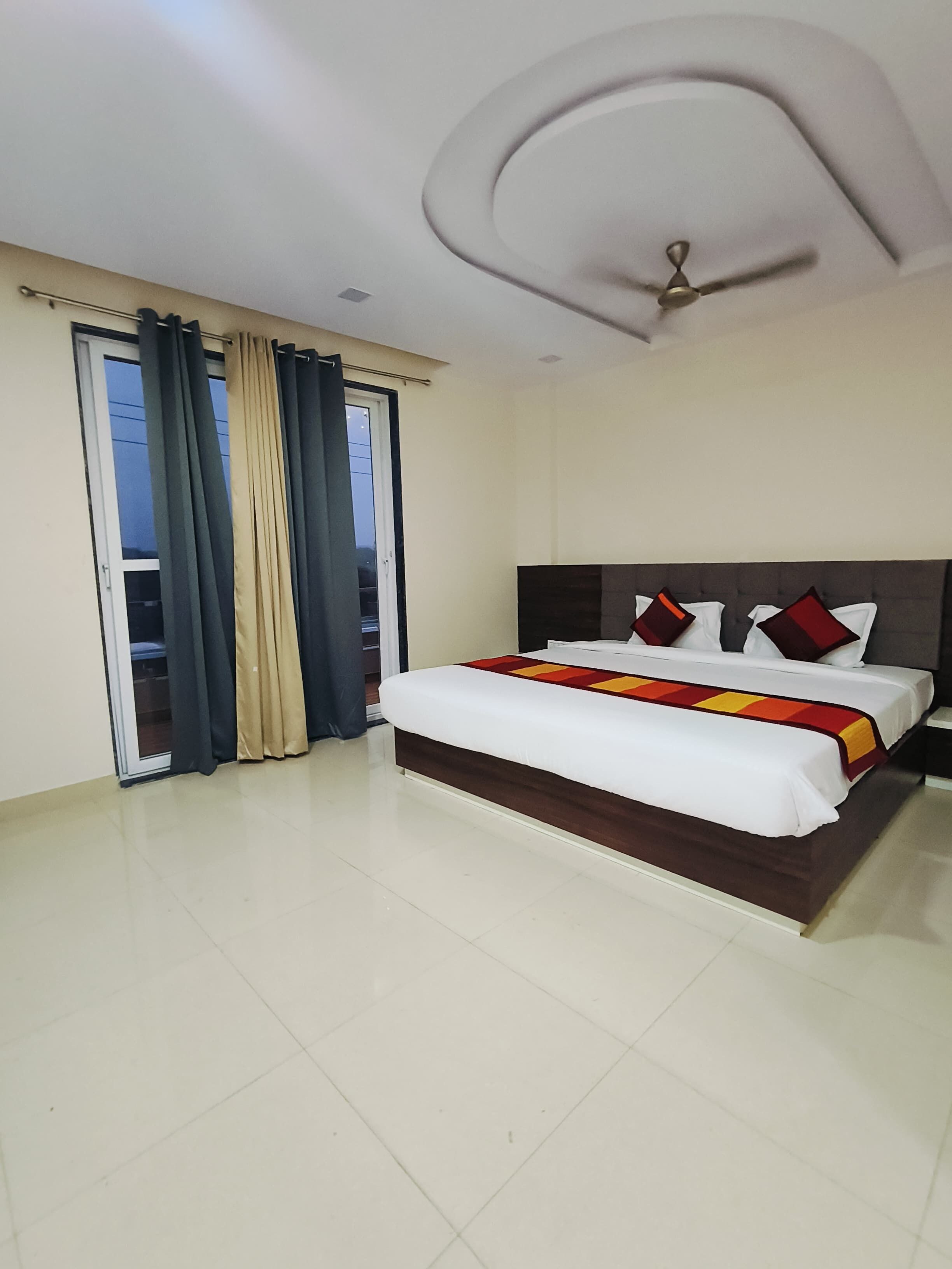 A hotel room with a bed, curtains, a ceiling fan, and a view through a window.