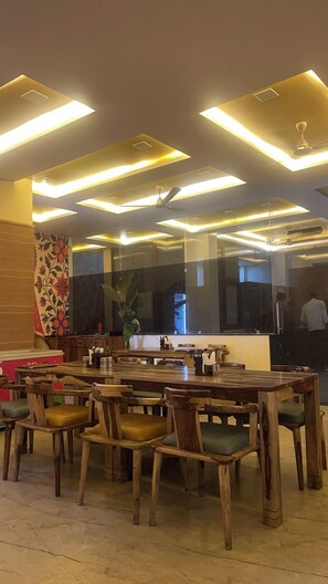 A restaurant interior with wooden tables and chairs, a large mirror, and modern ceiling lighting.