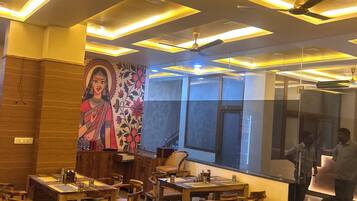 Interior de restaurante com mesas e cadeiras de madeira, um mural na parede e teto com iluminação embutida.