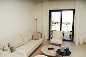Un salón con sofá, sillón, mesa de centro y vistas al exterior a través de un ventanal corredero.