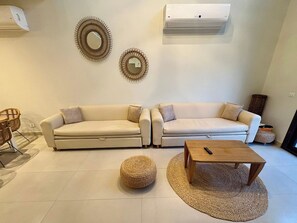 Ein Wohnzimmer mit zwei Sofas, einem Couchtisch, einem runden Hocker und Wanddekoration.