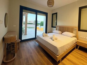 Ein Hotelzimmer mit Bett, einem kleinen Tisch, einem Stuhl, einem Fenster mit Jalousien und Blick ins Freie.