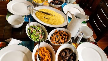 A dining table set with various dishes, including rice, salad, and meat, in a room with wooden furniture and a stone wall.